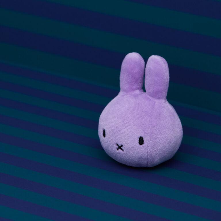 Purple Miffy plush toy on a striped background.