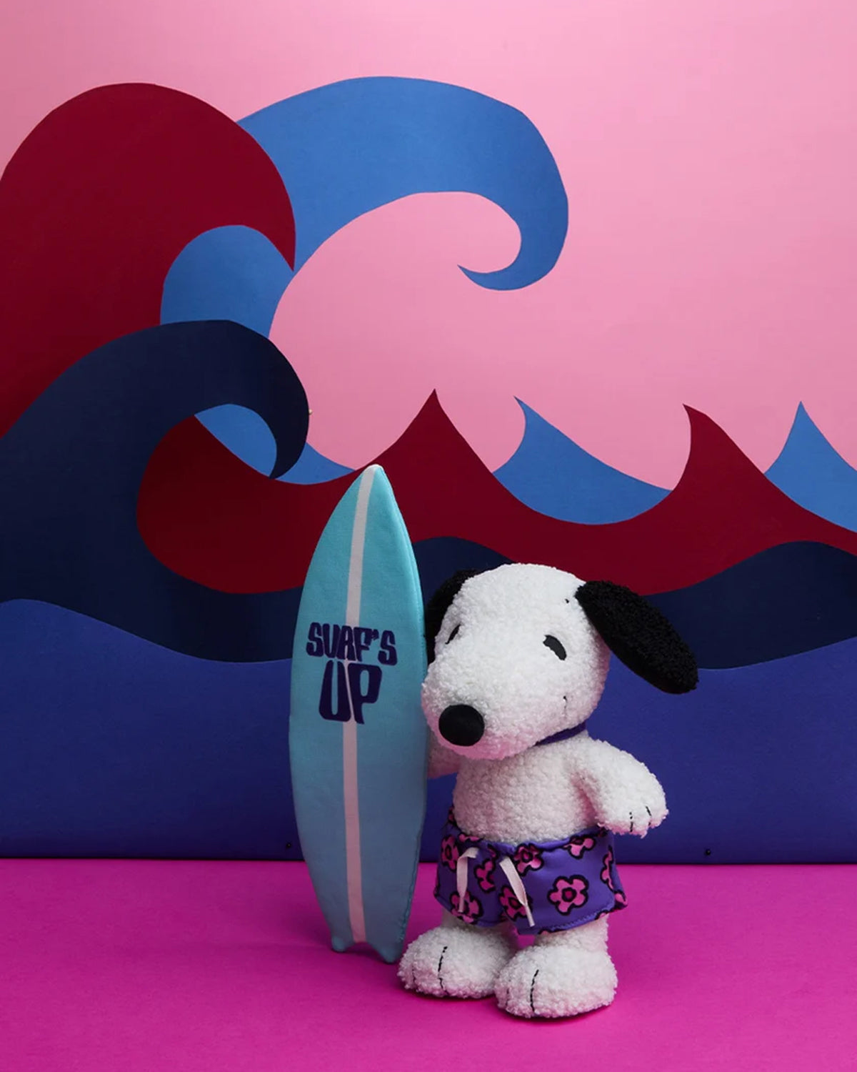 Stuffed Snoopy toy, surfboard, floral swim trunks, pink and blue wave backdrop.