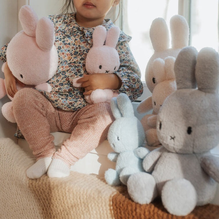 A child holding plush Miffy rabbits in pastel colors.