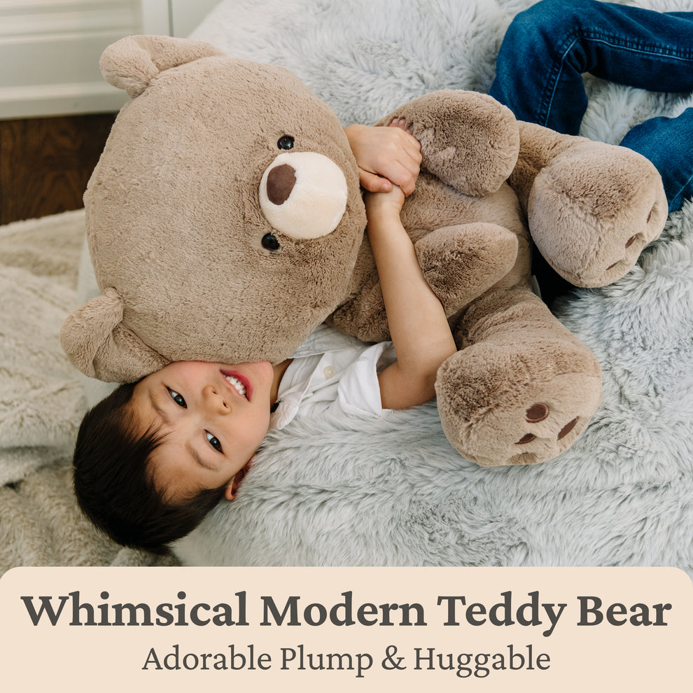 A child lying on a fur rug while hugging a large brown teddy bear.