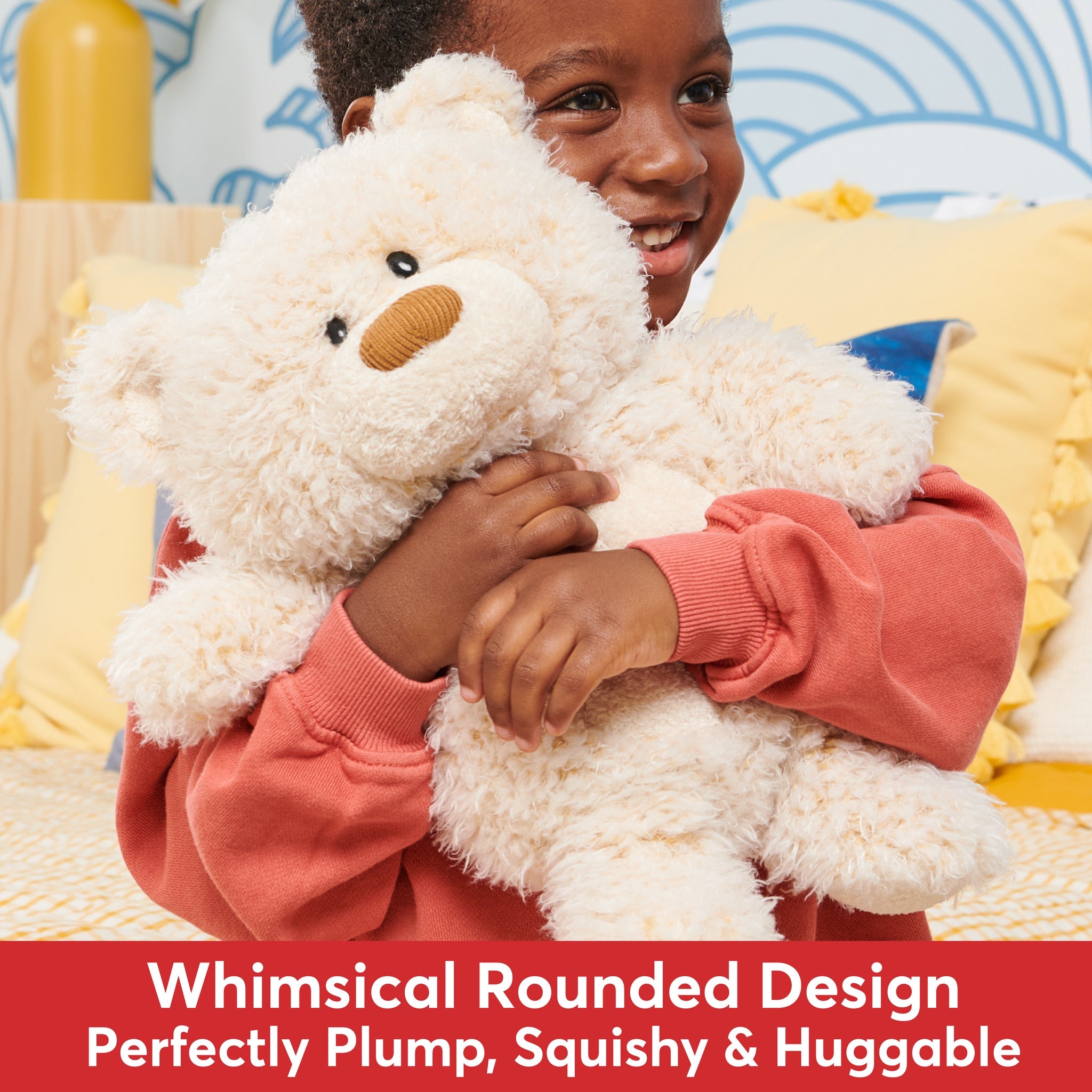 Boy holding a cream-colored teddy bear while wearing a salmon-colored sweatshirt.