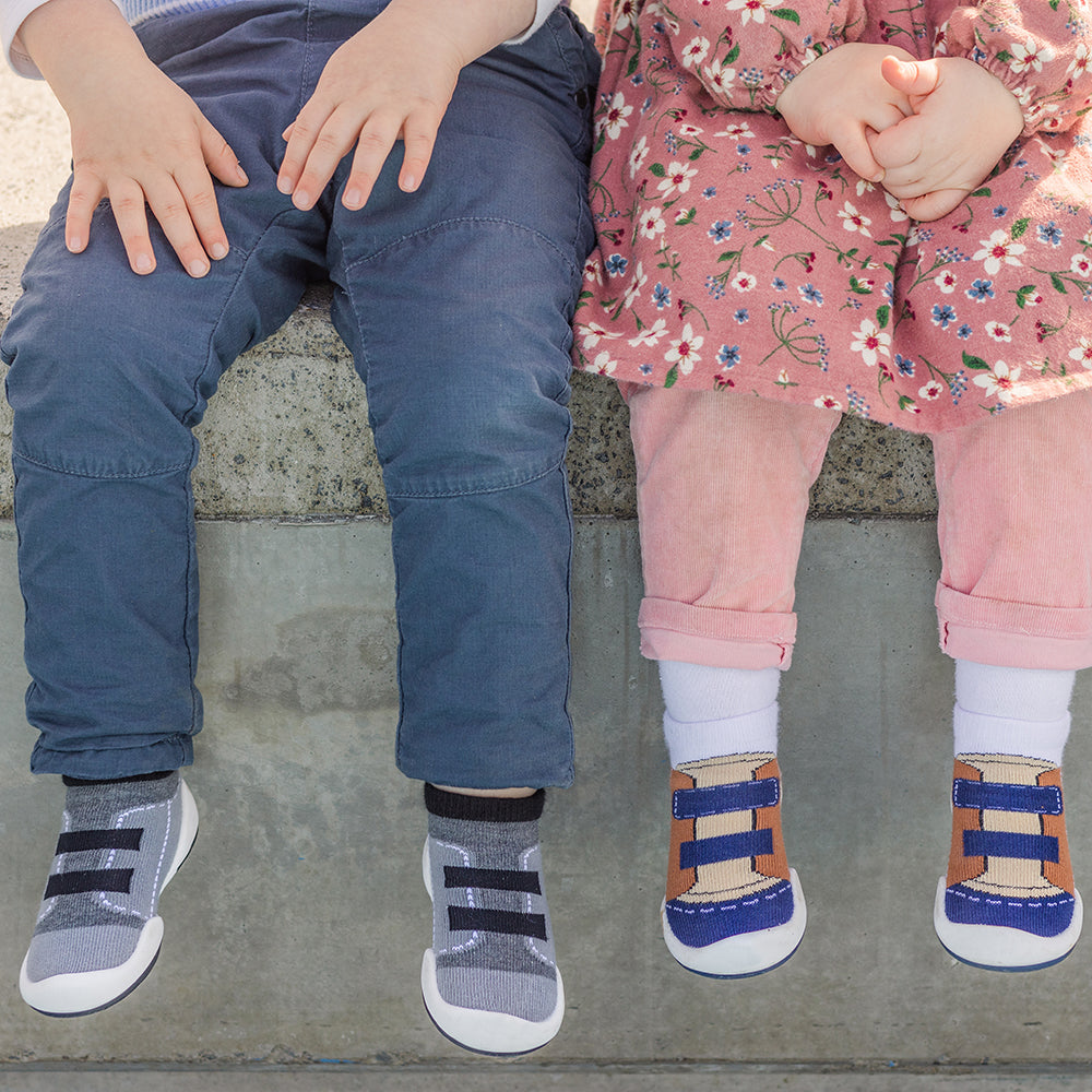 Two children sitting together, wearing pants and shoes.