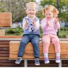 Two toddlers sitting on a wooden bench clapping, wearing sweaters and shoes.