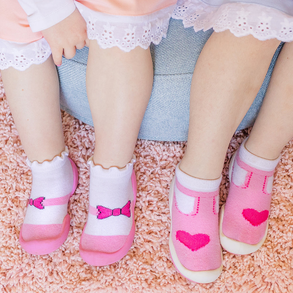 Two children with bare legs wearing pink and white socks on a shaggy pink rug.