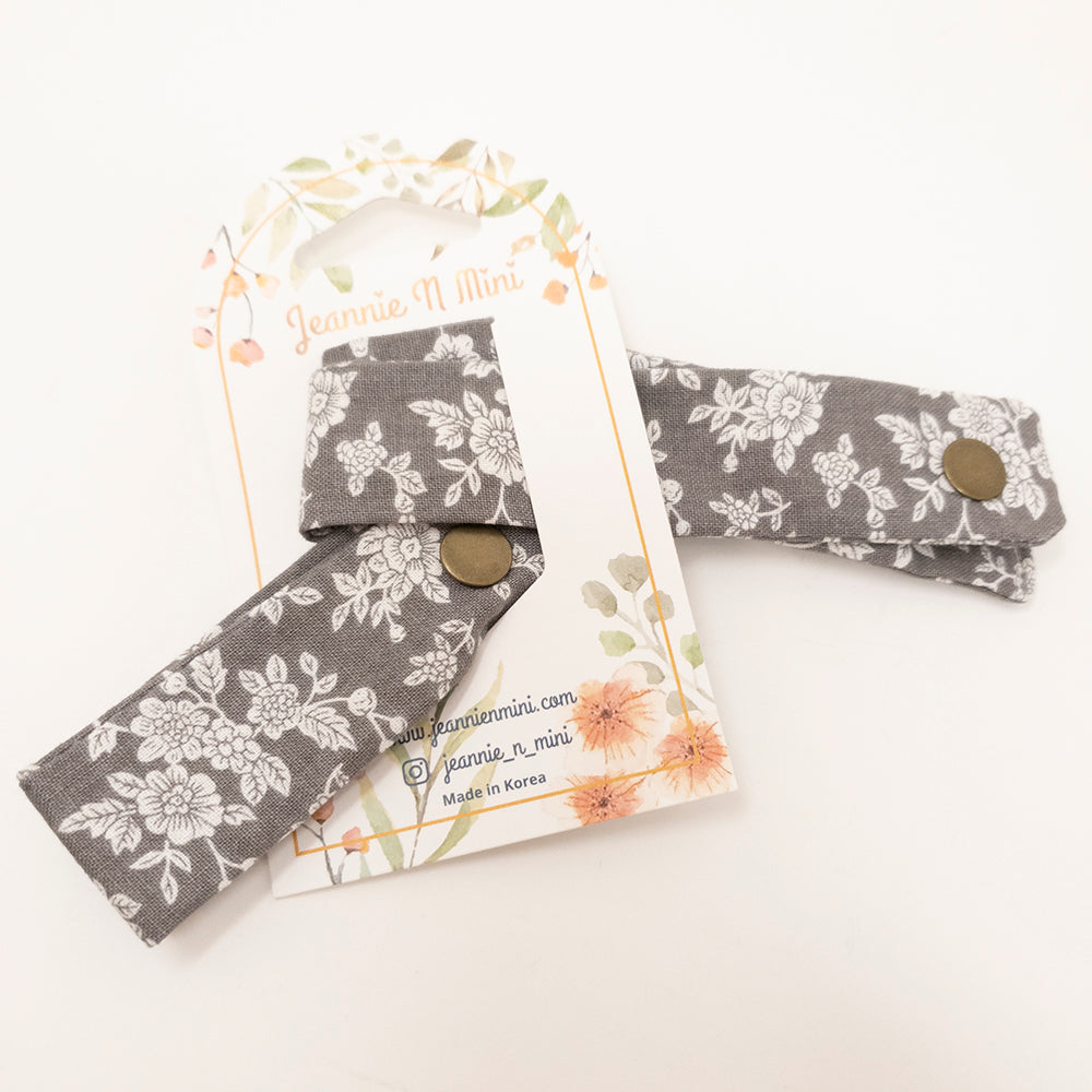 Gray floral patterned wrist straps with bronze snaps on decorative card.