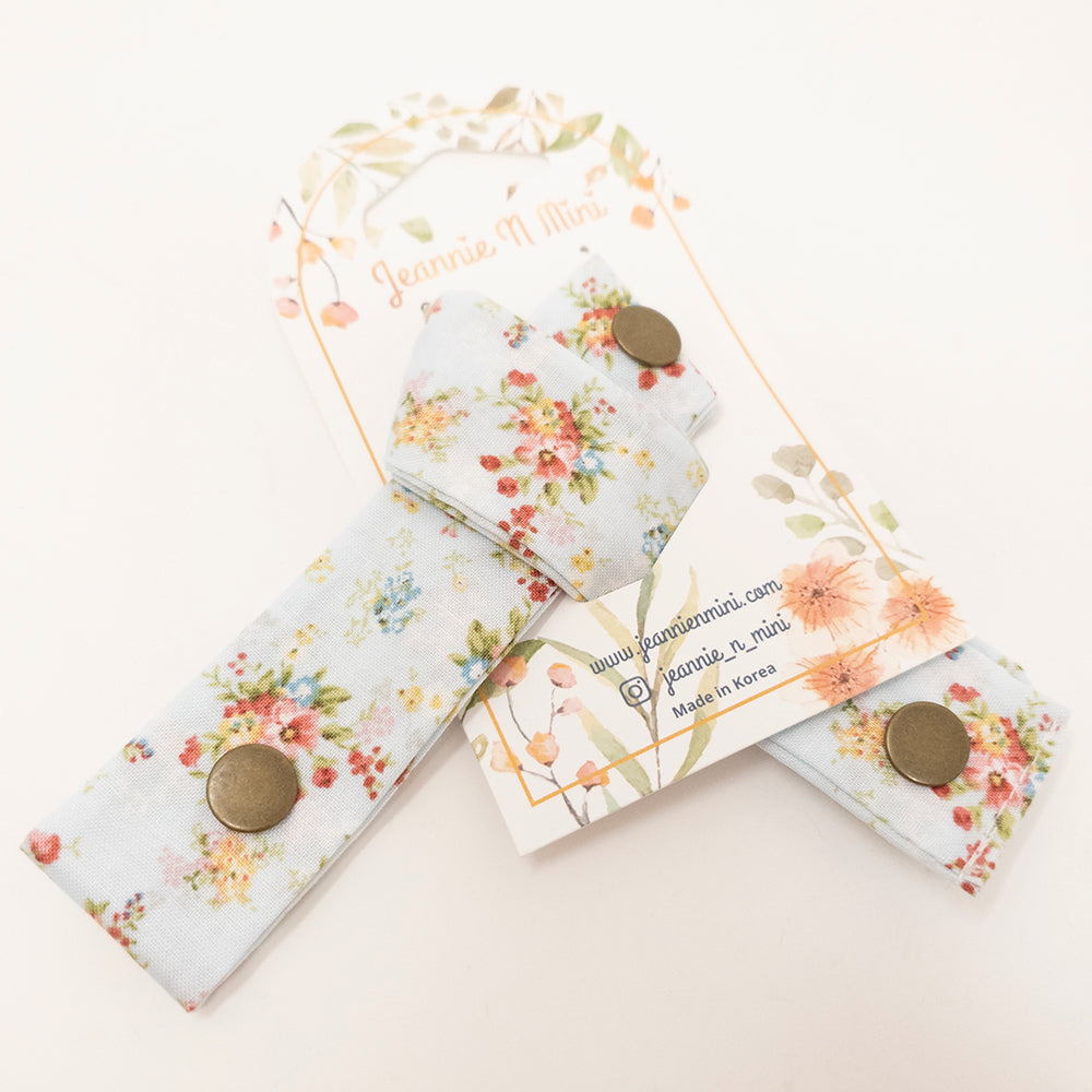 Light blue floral fabric hair tie with bronze buttons on a card with watercolor flowers.