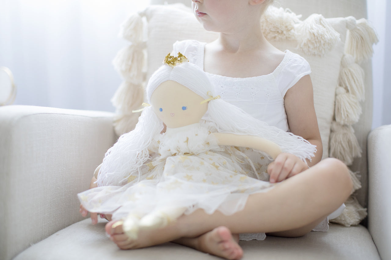 Child holding a rag doll in a chair.