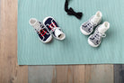 Two pairs of baby sneaker socks and a black bow tie on a turquoise mat, placed on a wooden surface.