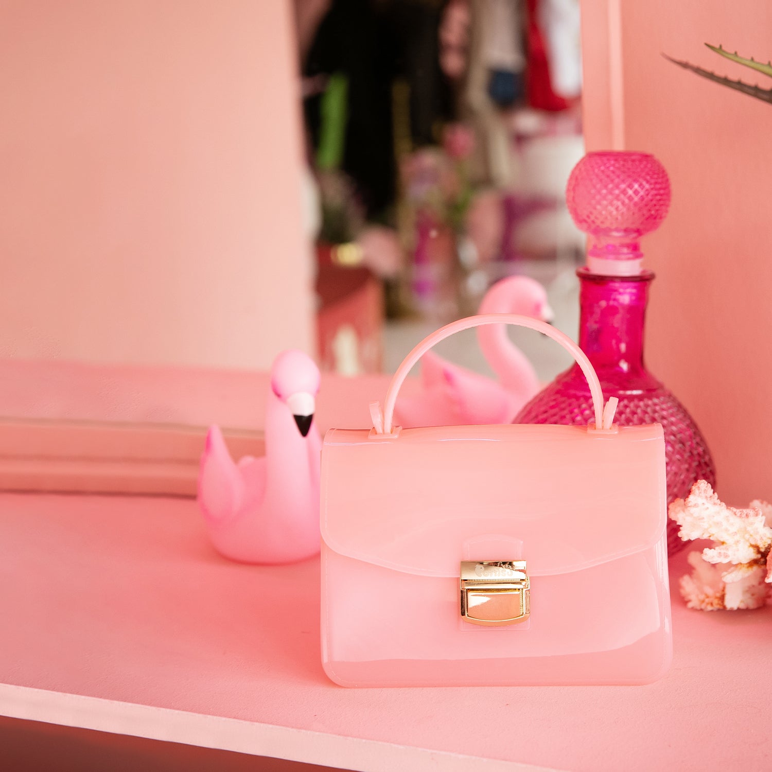 Close-up of pink purse, flamingo, and glass bottle on pink shelf.