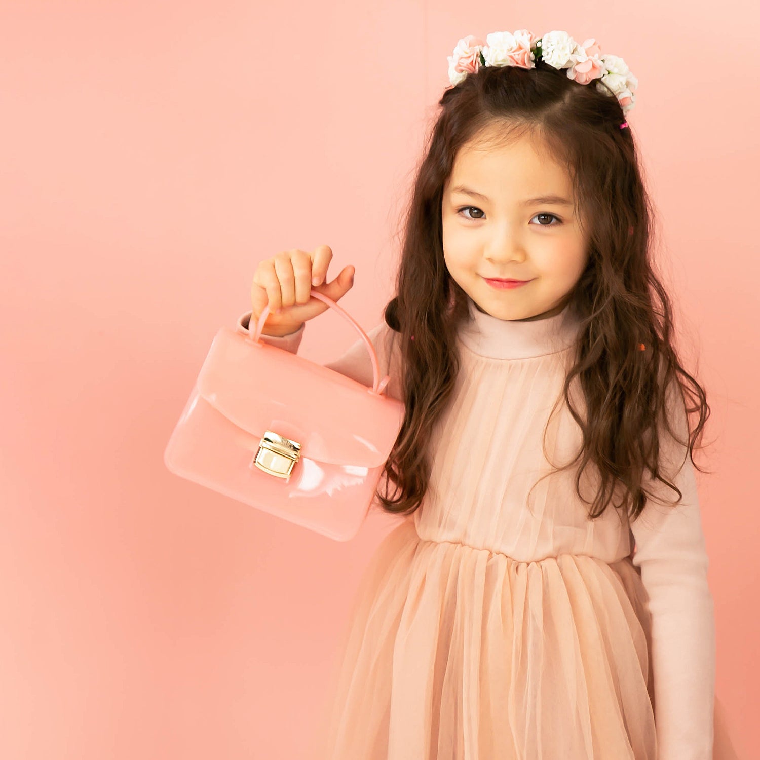 Girl in pink dress holding pink purse with flower crown.