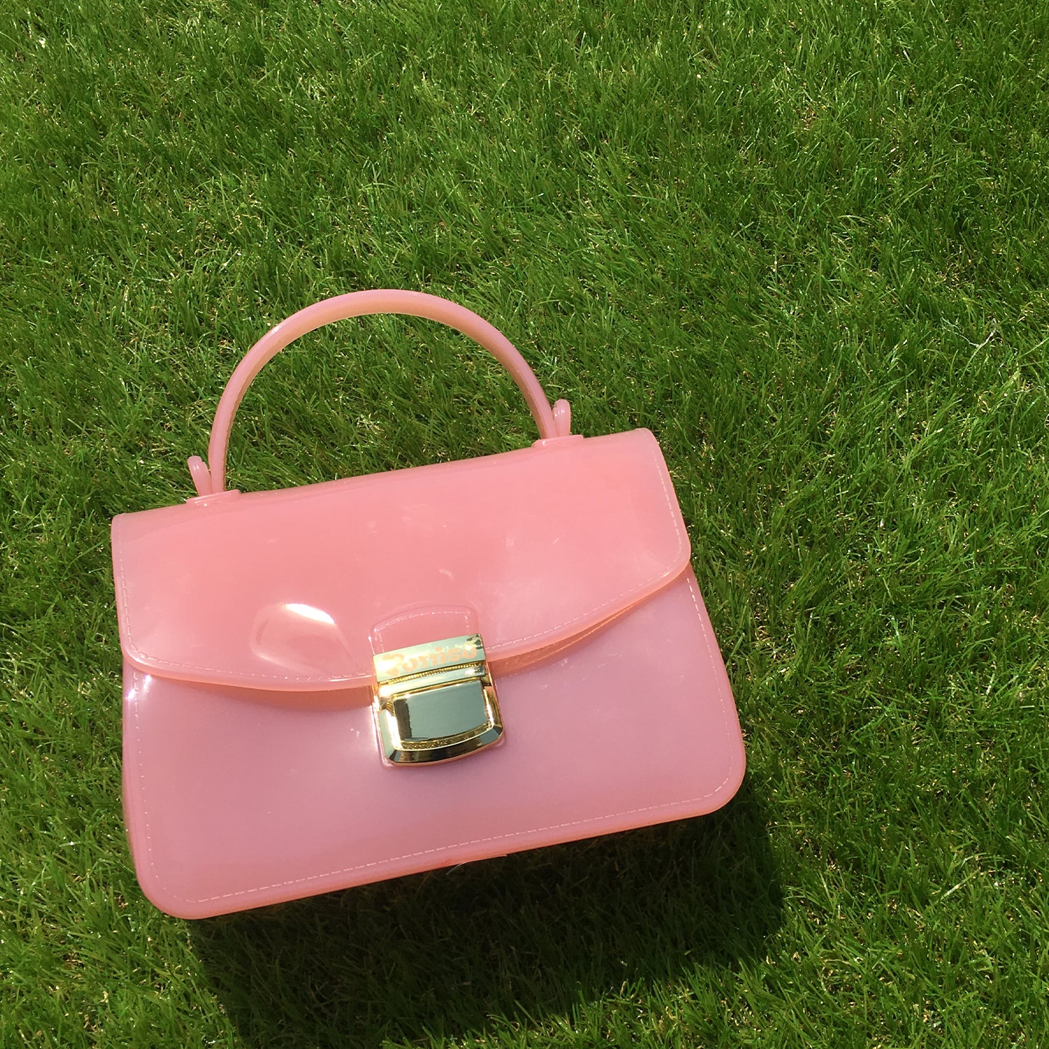 A shiny pink purse with a gold clasp lies on green grass.