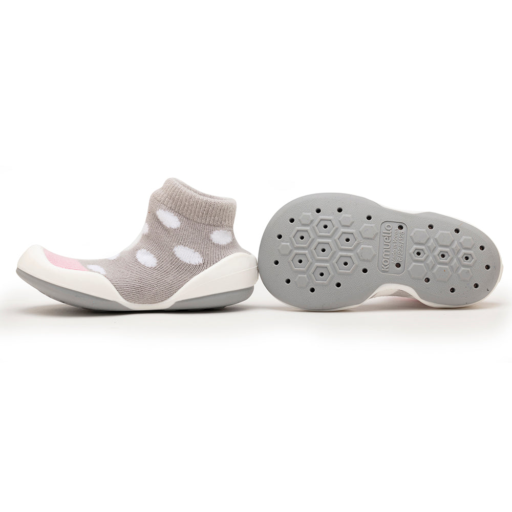 Two baby sock shoes, one with a gray sock with white polka dots and a white sole, and the other showing the gray sole with patterned holes.