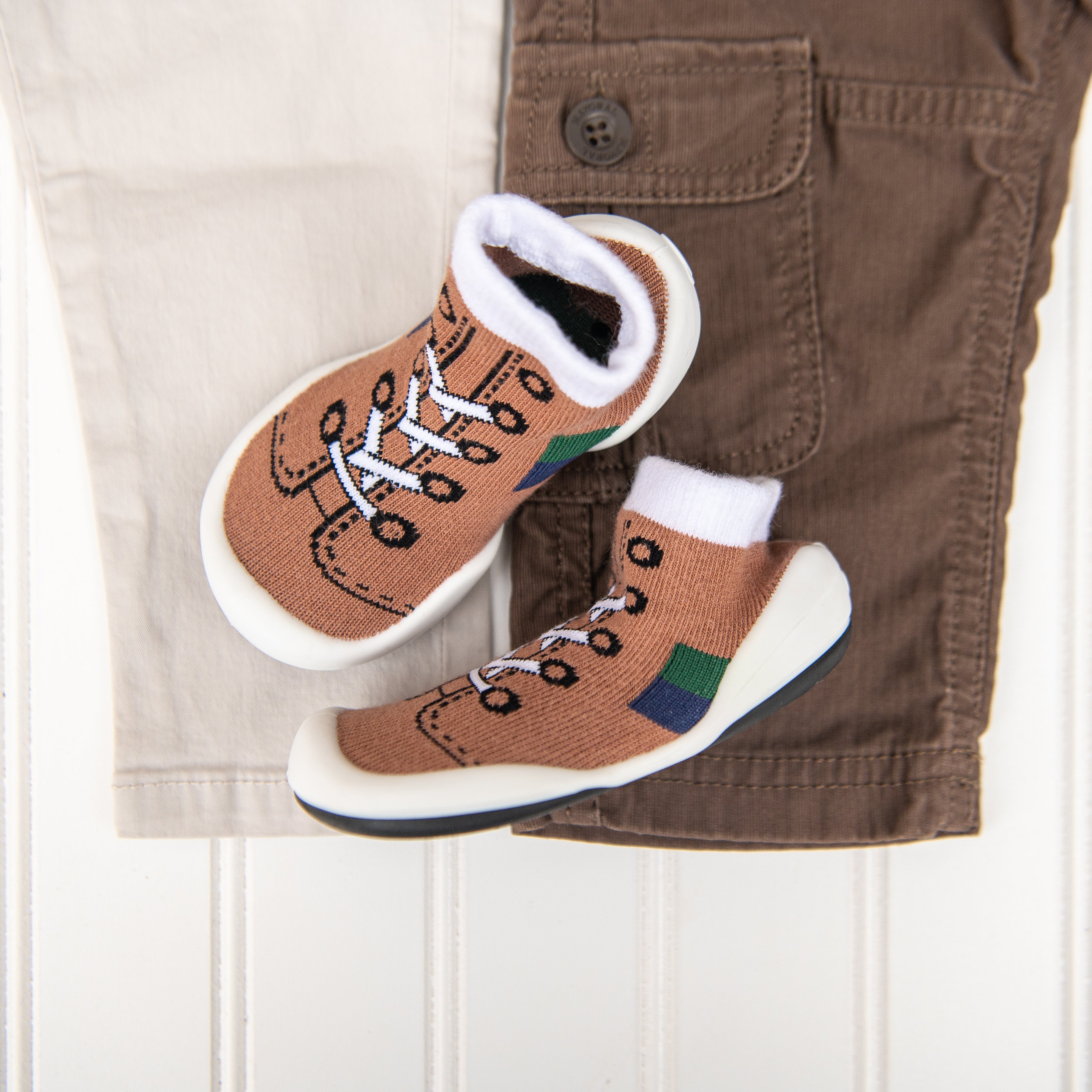 Two baby shoes lie on top of tan and brown pants.
