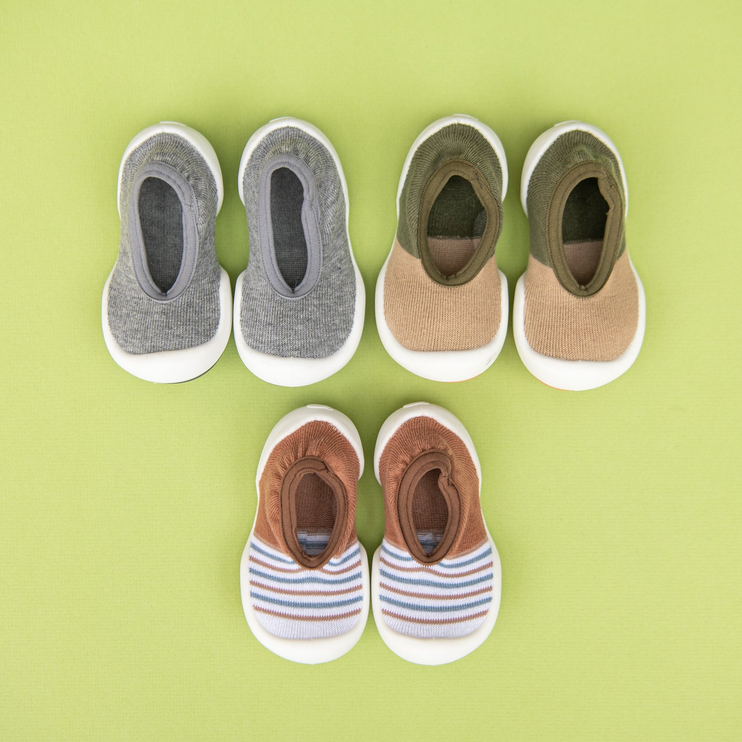 Five pairs of baby shoes on a green background.
