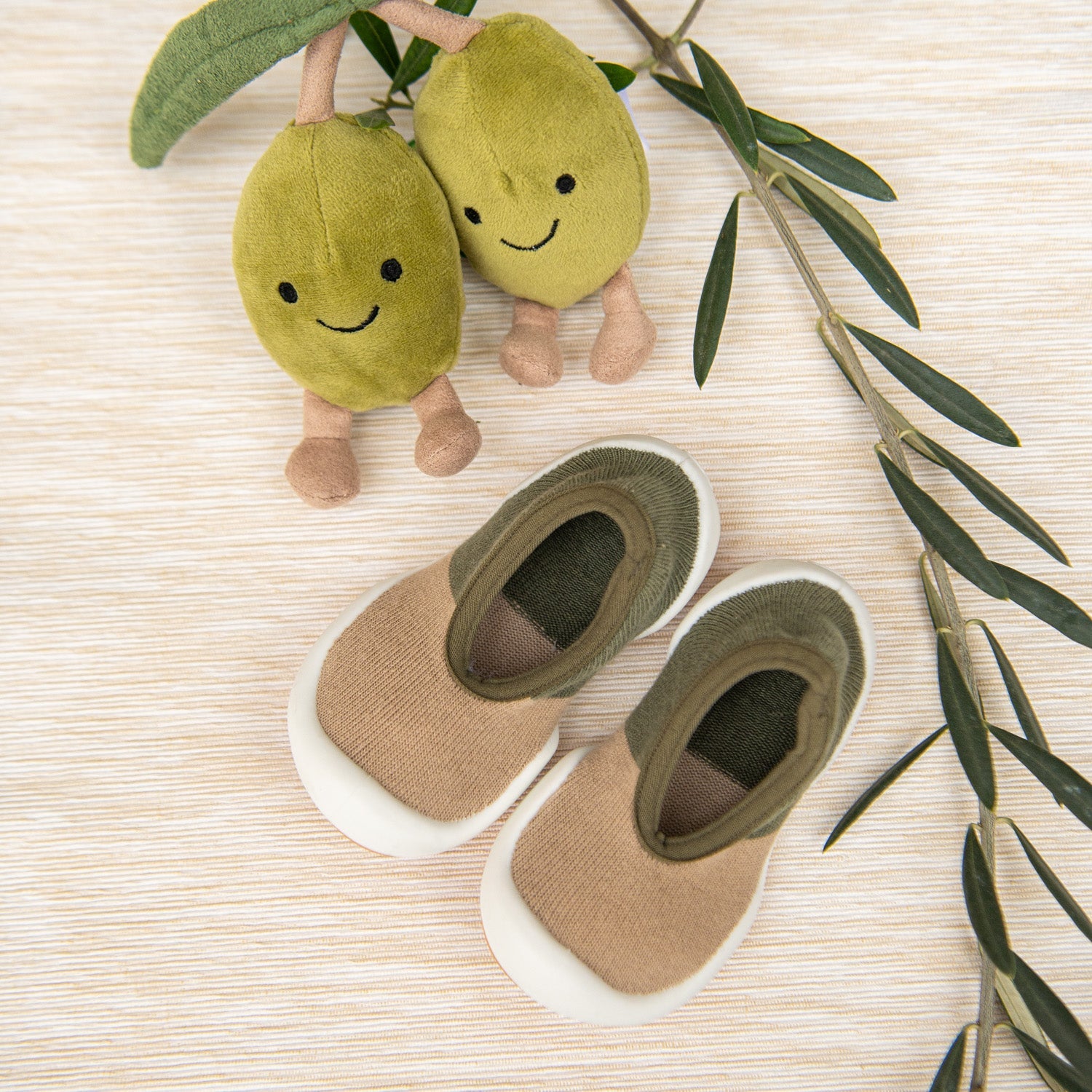 Two stuffed olives with olive branch next to baby sock shoes.