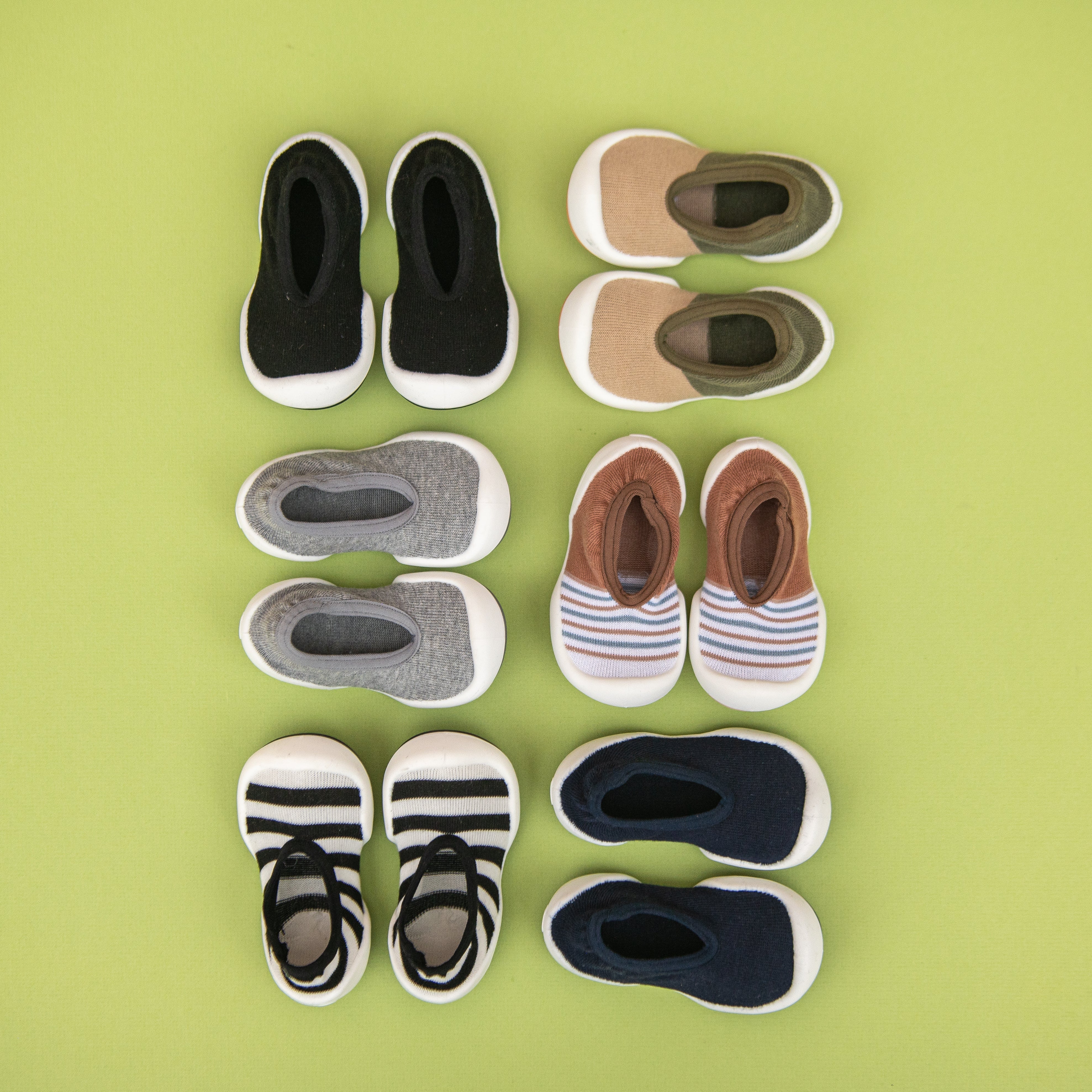 Several pairs of colorful baby shoes on a green background.