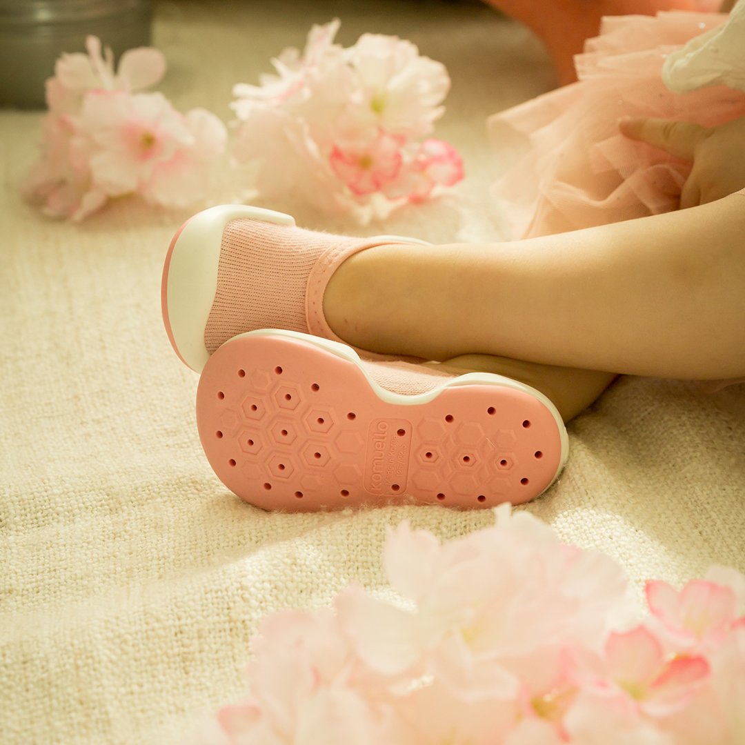 Child's pink sock shoes, pink tutu, pink flowers, white carpet.