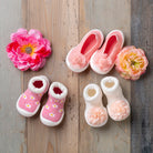 Three pairs of baby shoes and two pink flower accessories on a wooden background.