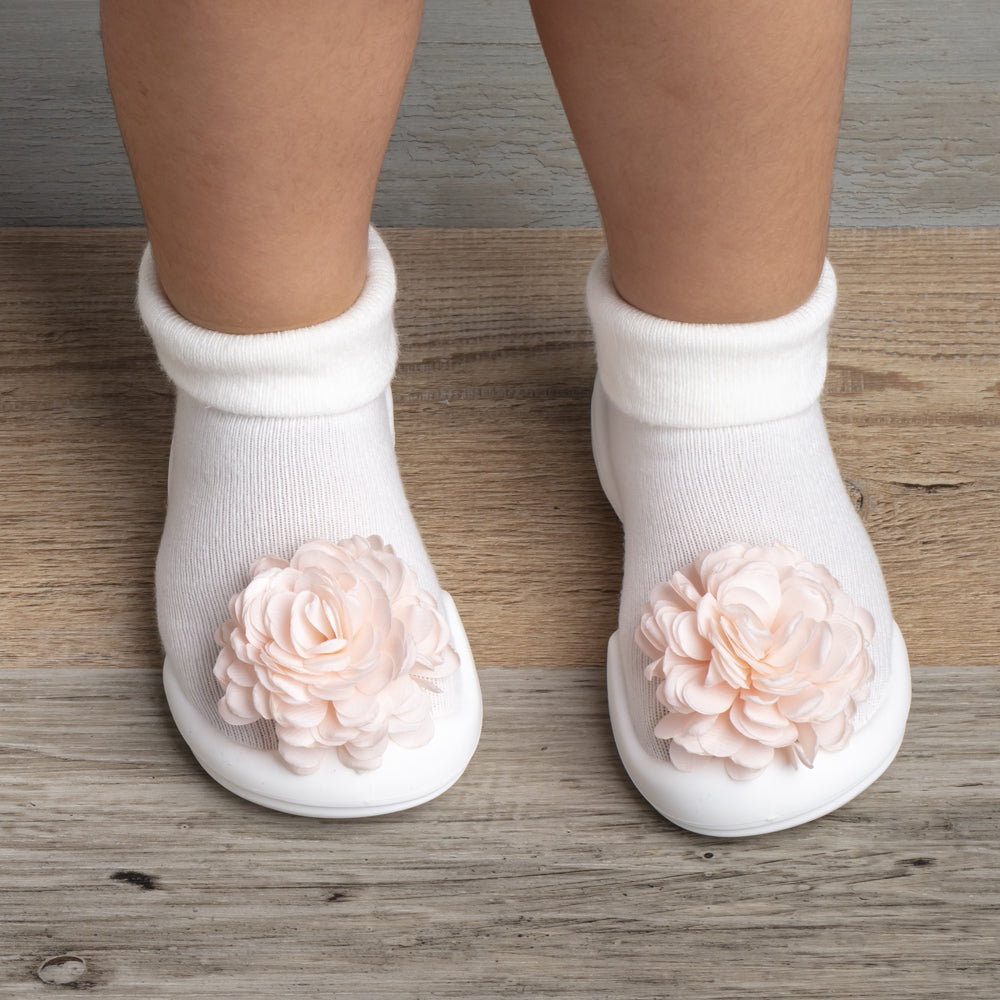 Close-up of baby's feet in white socks with peach floral embellishments on a wood-look floor.