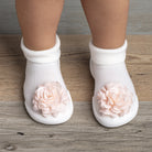 Close-up of baby's feet in white socks with peach floral embellishments on a wood-look floor.