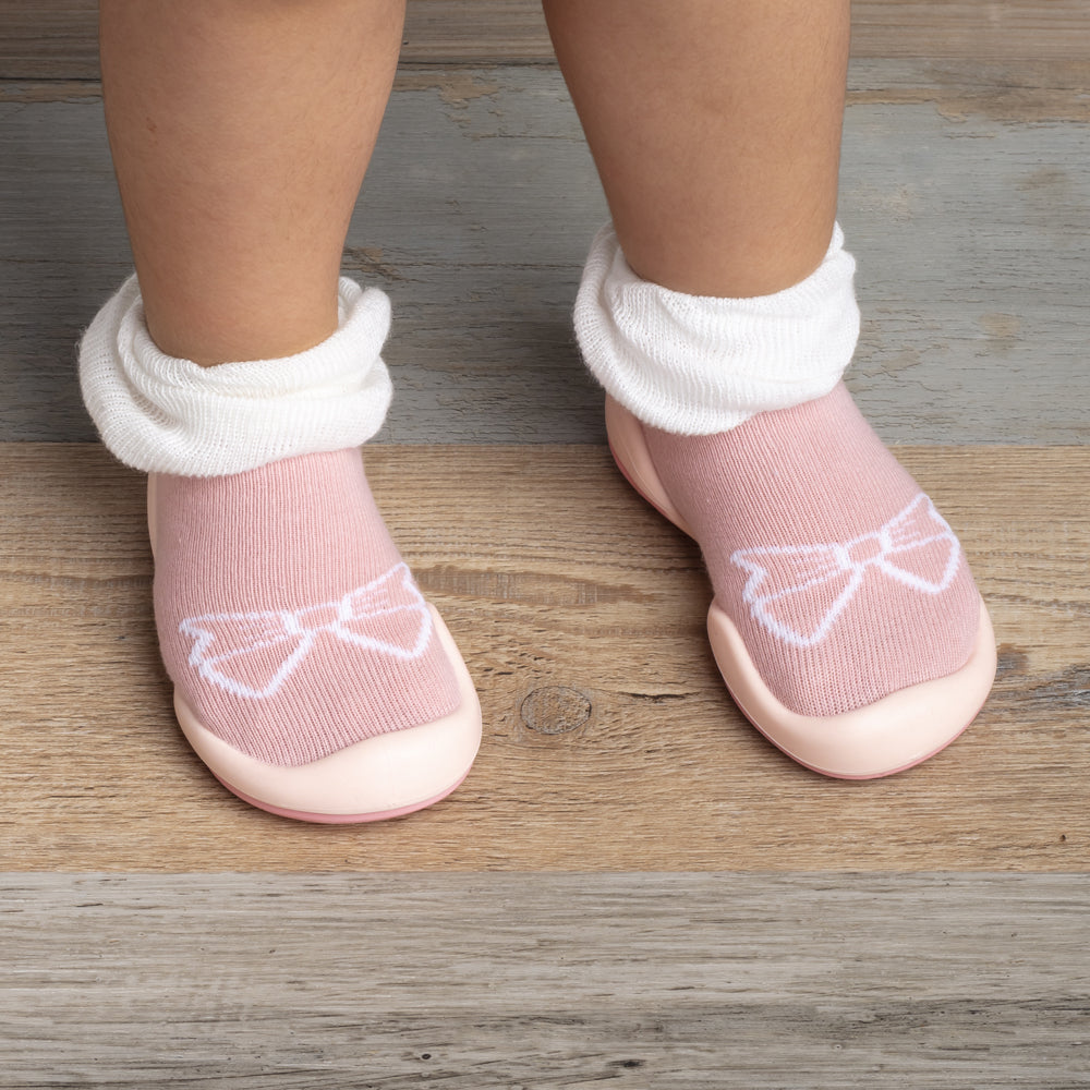 Close-up of baby feet wearing pink and white bow-adorned socks on a wooden surface.