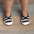 Close-up of baby's feet in black and white striped shoes on a wood floor.