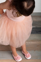 Overhead view of a child in a pink dress with a tulle skirt and matching pink flower-embellished shoes.
