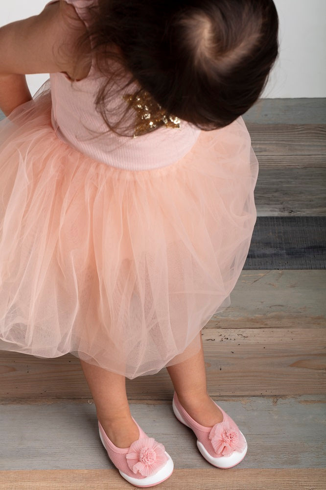 Overhead view of a child in a pink dress with a tulle skirt and matching pink flower-embellished shoes.