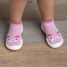 Two feet wearing pink sock-shoes with pig faces on a wooden floor.