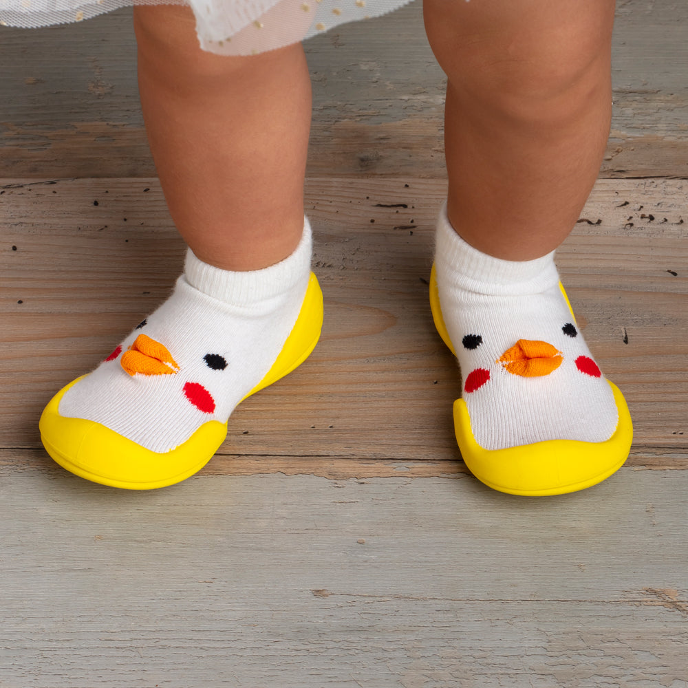 Child's feet in white sock-shoes with yellow soles, chick face design on top.