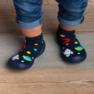 A child wearing blue jeans and space-themed sock-shoes on a wooden floor.
