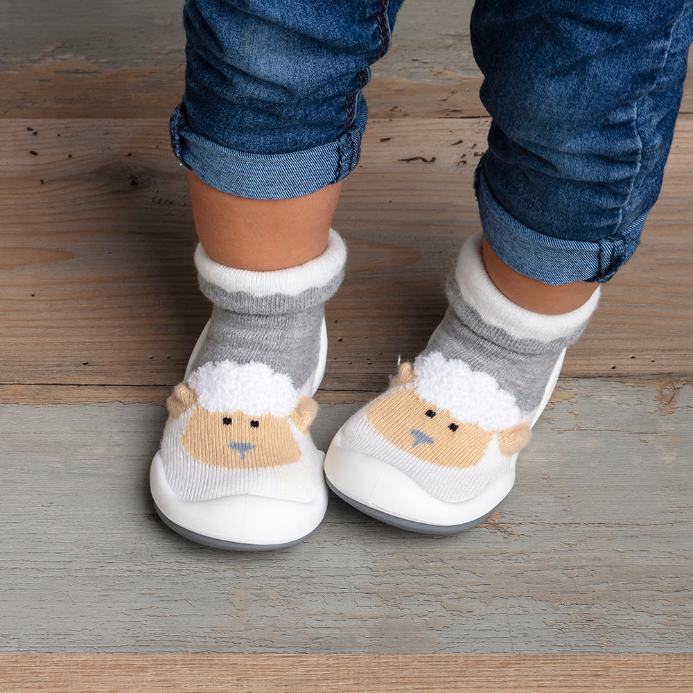 Baby wearing sheep-themed sock shoes and jeans.