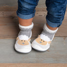 Baby wearing sheep-themed sock shoes and jeans.