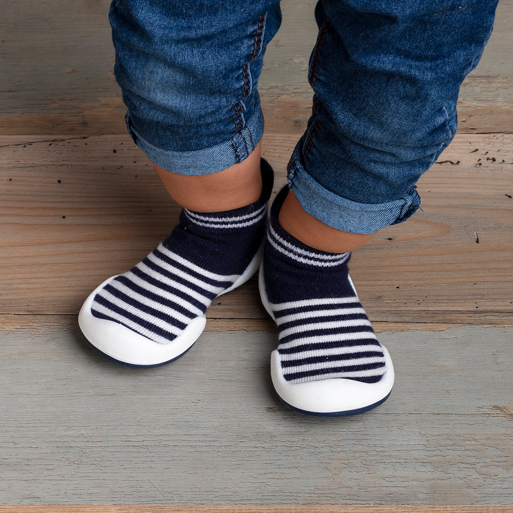 Child's feet wearing striped socks with attached white shoe soles, blue jeans, on a wood floor.