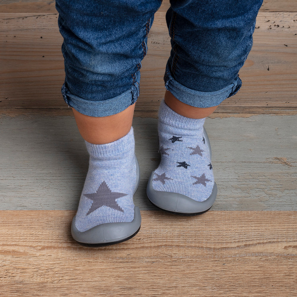 A toddler wearing blue jeans and light blue socks with grey stars on a wood floor.