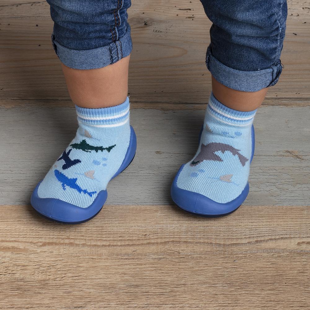 Close-up of a child's feet wearing blue sock shoes with shark patterns, standing on a wooden floor.
