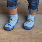 Close-up of a child's feet wearing blue sock shoes with shark patterns, standing on a wooden floor.