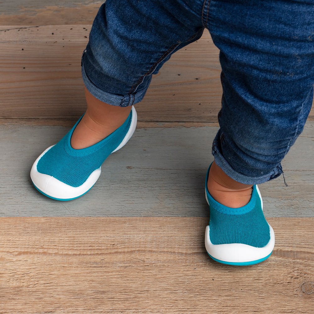 A baby in jeans and blue shoes on a wood floor.