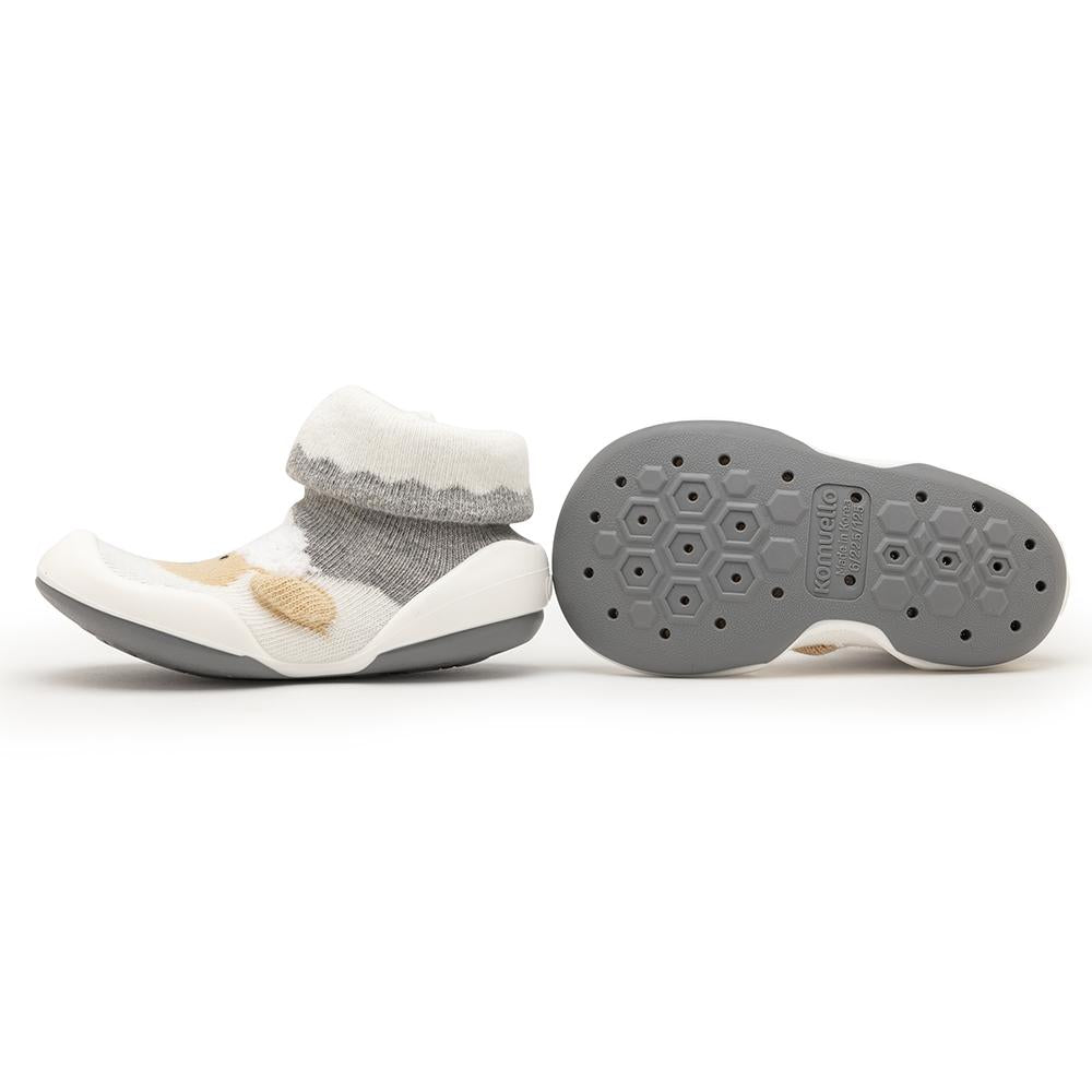 Two baby shoes, one upright with gray and white sock-like upper and tan accent, and a gray and white sole, next to its outsole showing a honeycomb pattern.