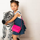 A young girl with a pink purse and denim dress hugs a stuffed zebra.