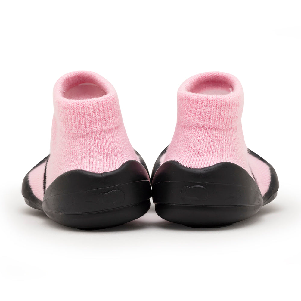 Two pink sock-like baby shoes with black rubber soles, viewed from the back.