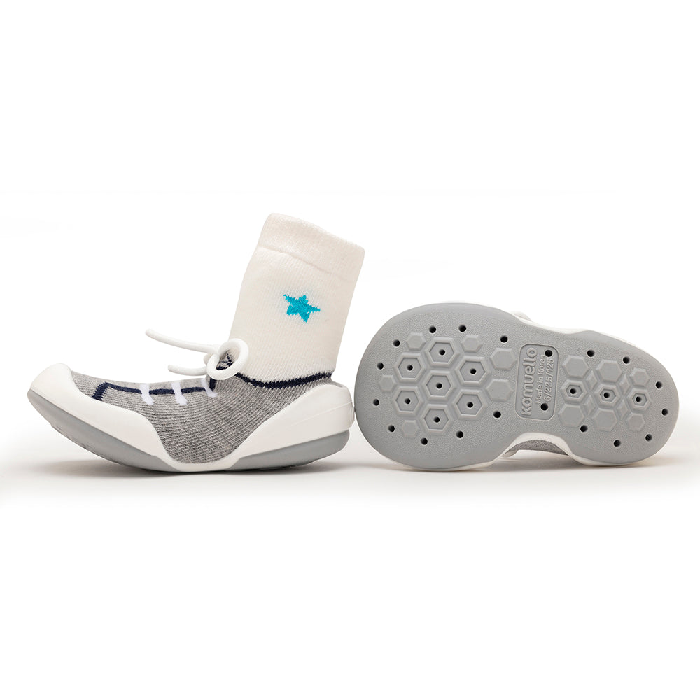 One gray and white baby sock shoe with a white sock and a star, next to its grey sole.