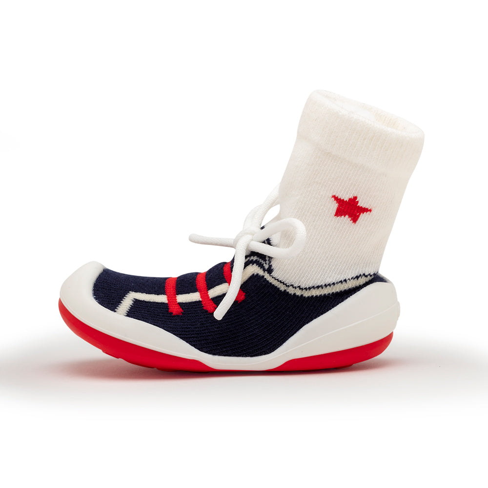 A child's shoe that looks like a sock with a red star and faux red laces over navy blue, and white soles.