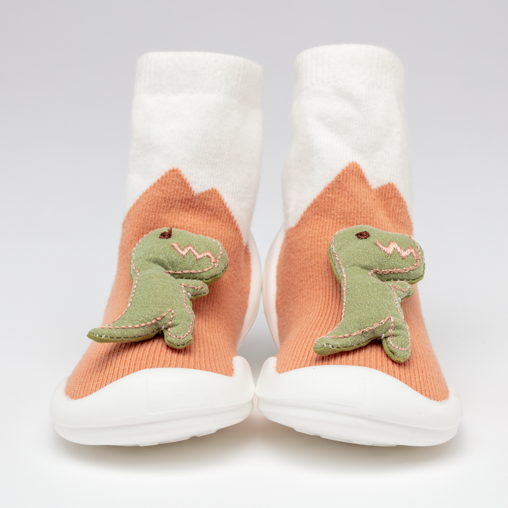 Pair of orange and white sock shoes with green dinosaur accents.