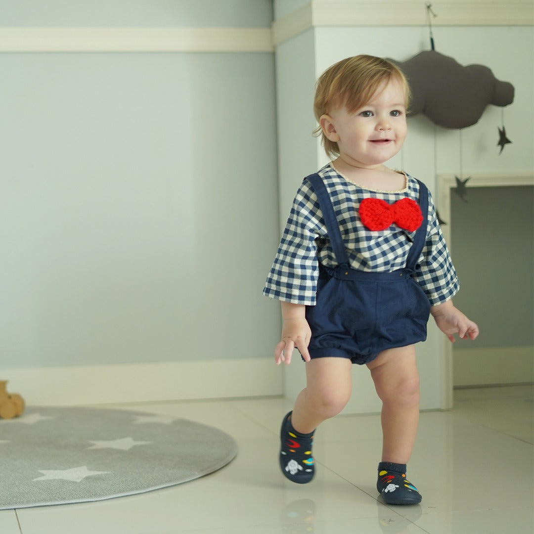 Toddler wearing plaid shirt, blue overalls, red bow tie, and patterned shoes.