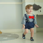 Toddler wearing plaid shirt, blue overalls, red bow tie, and patterned shoes.