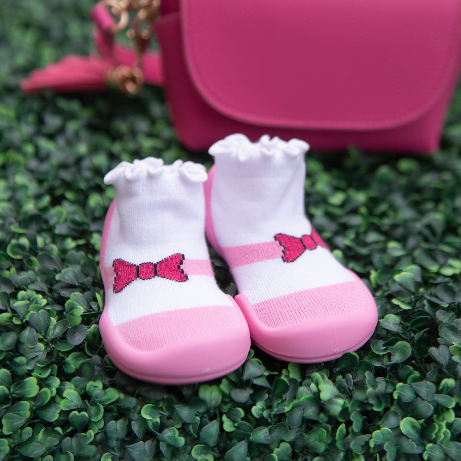 Pair of pink and white baby shoes with bows on green artificial grass.