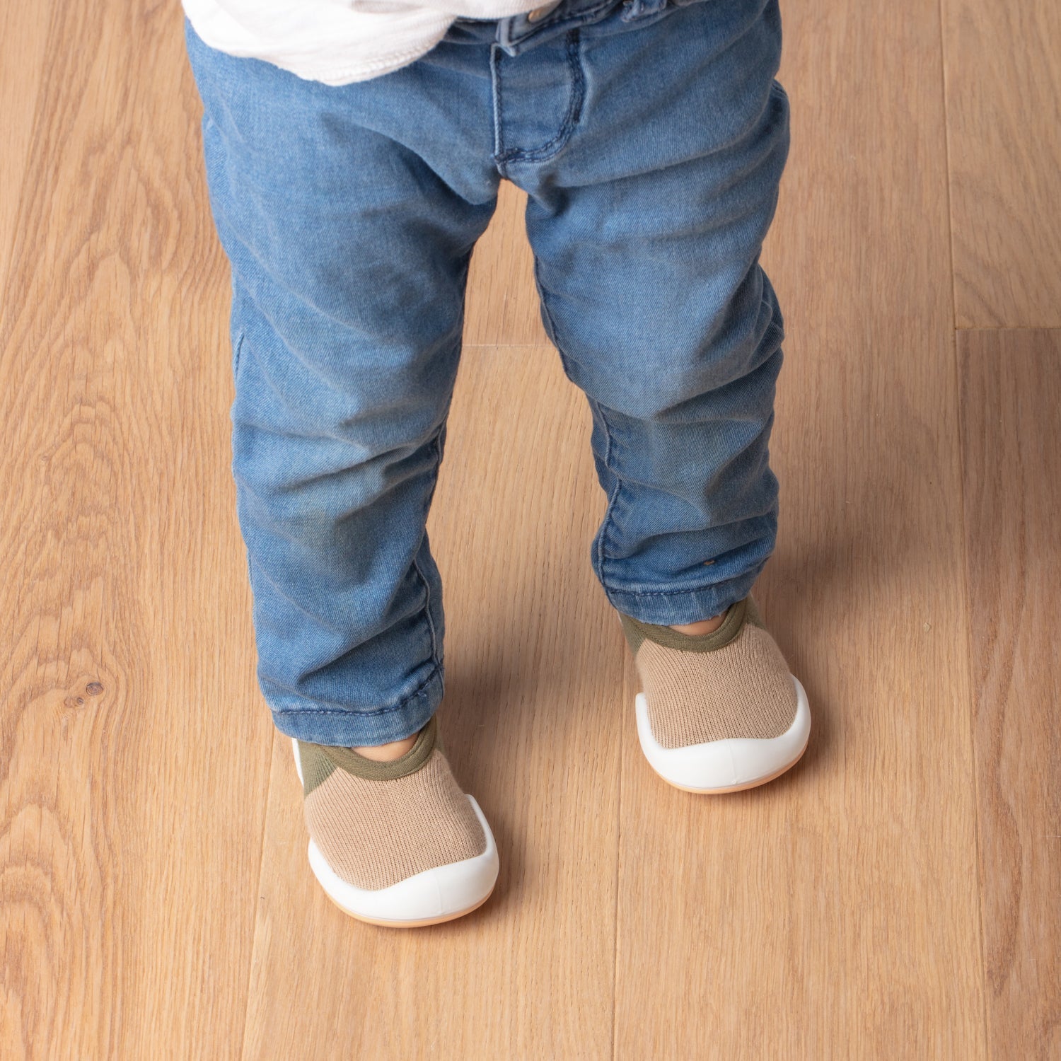 Child wearing jeans and tan shoes on a wood floor.