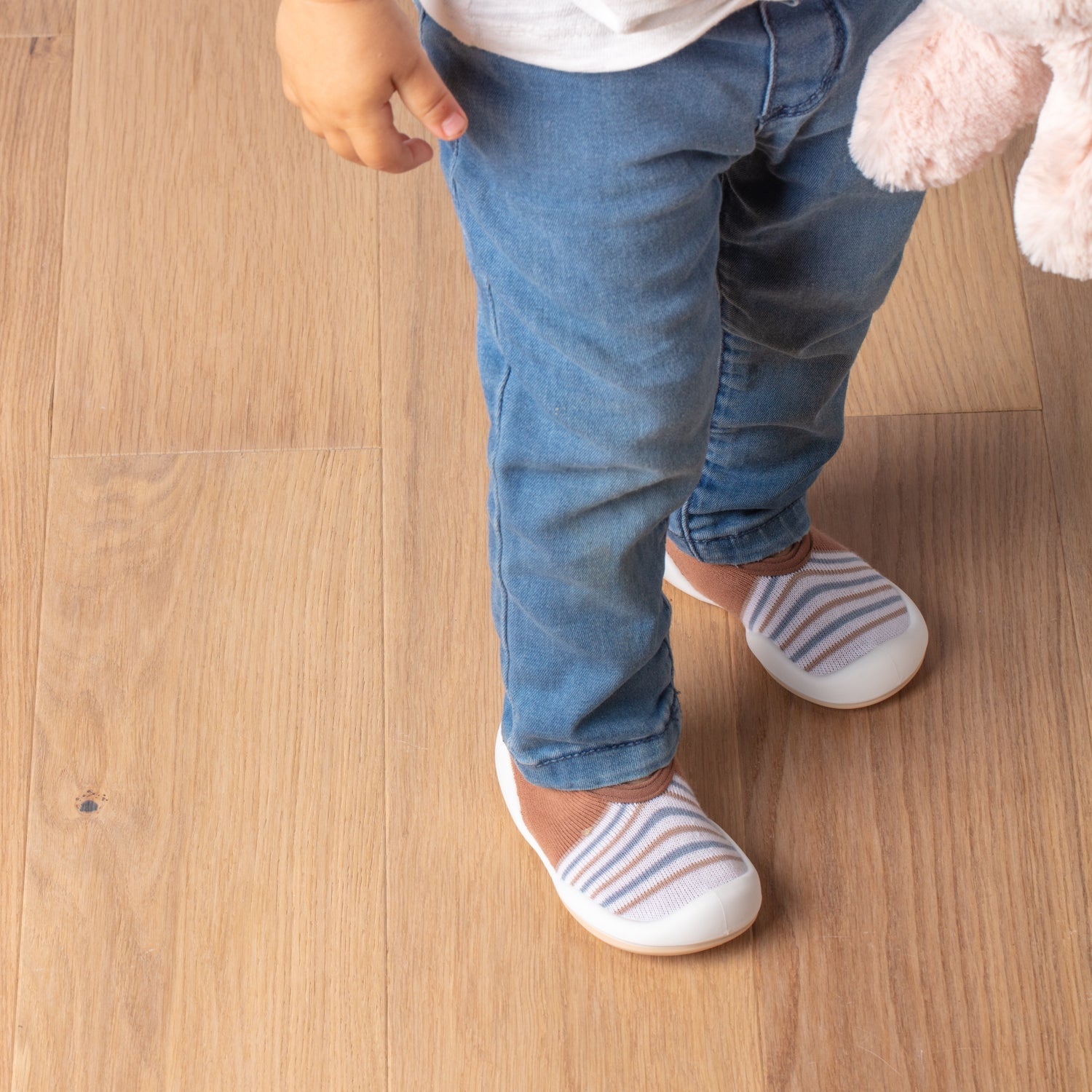 Child in jeans and striped shoes standing on a wooden floor.