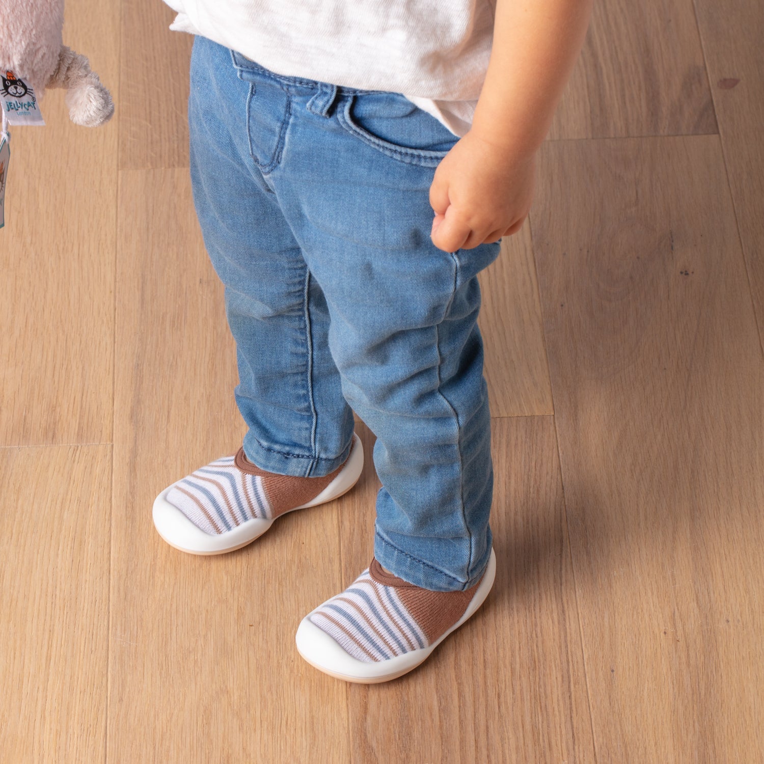 Child in jeans and striped shoes on wood floor.